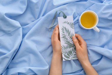 Yatağında çay ve kitap ayracı olan bir kadın.