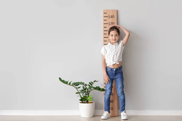 Little girl measuring height near light wall
