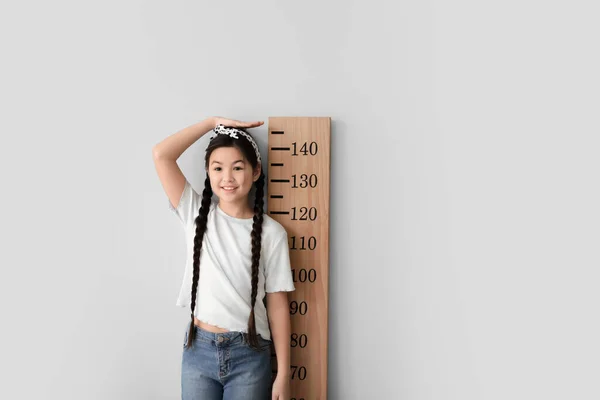 Little girl measuring height near light wall