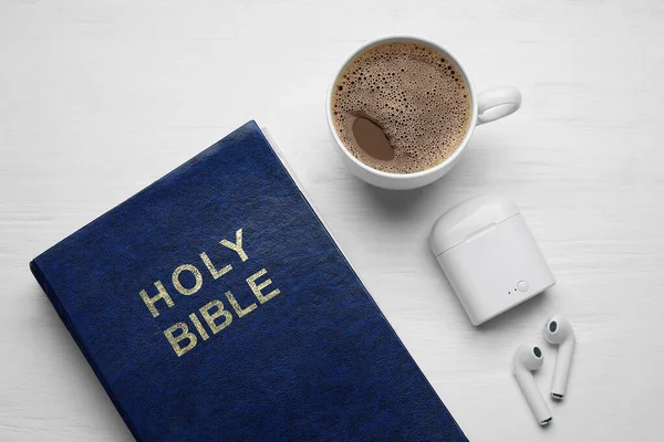 Holy Bible, cup of coffee and earphones on light wooden background