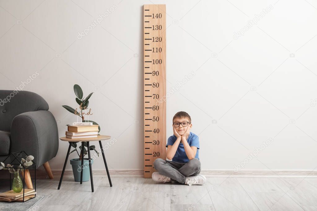 Little boy sitting near big ruler for measuring height at home