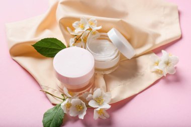 Renkli arkaplanda krema kavanozları ve yasemin çiçekleriyle kompozisyon