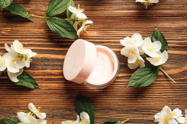 Tahta arka planda bir kavanoz krema ve yasemin çiçeği.