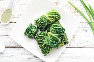 Doldurulmuş lahana yapraklı tabak ve açık ahşap zemin üzerine sos.