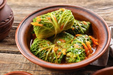 Doldurulmuş lahana yaprakları ve ahşap arka planda domates sosu olan bir kase.