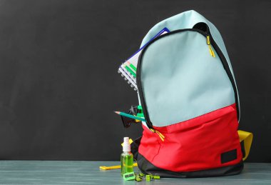 Okul çantası ve kırtasiye malzemesi tahtanın yanındaki masada.