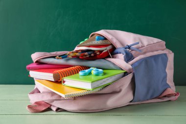 Okul çantası ve kırtasiye malzemesi tahtanın yanındaki masada.