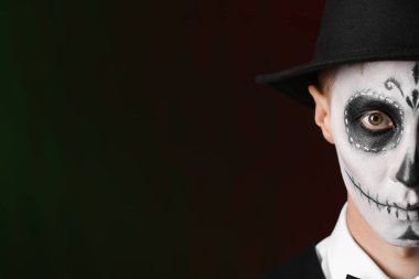 Meksika Ölüler Günü 'nde (El Dia de Muertos) yüzünde boyalı kafatası olan genç adam koyu arkaplana karşı