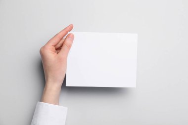 Gri arka planda boş kağıt tutan kadın, yakın plan.