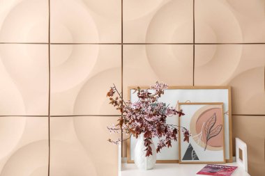 Renk duvarının yanındaki masada çiçek açan dalları olan vazo.