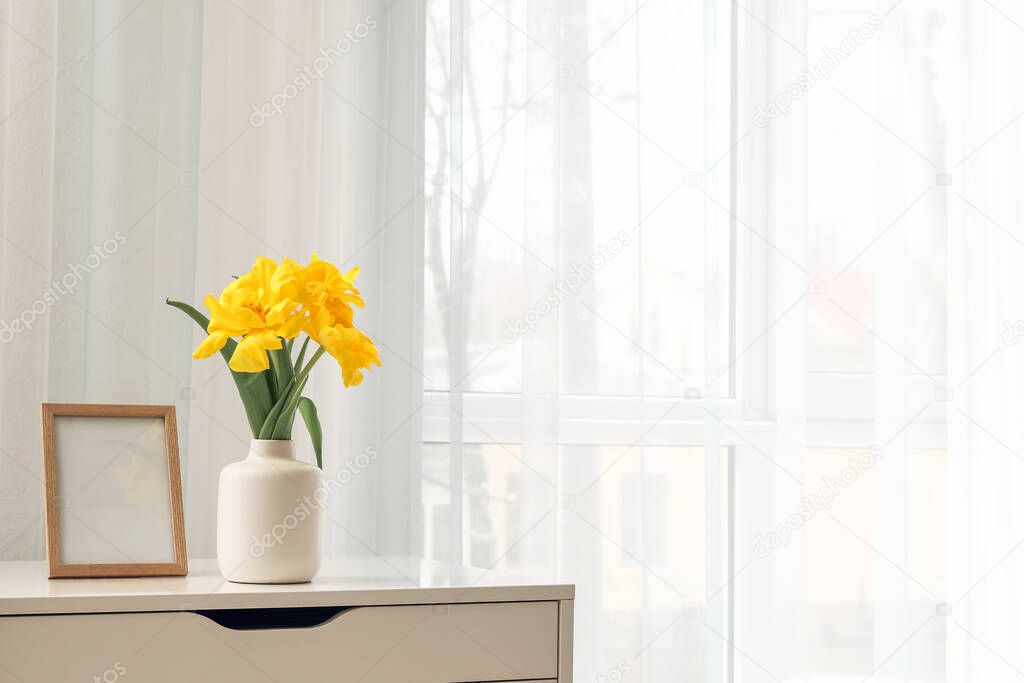 Vase with beautiful flowers and frame on shelf near window