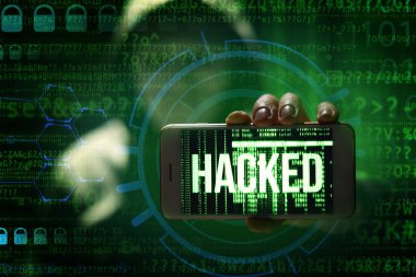 Bilgisayar korsanı cep telefonunu koyu arkaplana karşı ekranda HACKED sözcüğüyle tutuyor