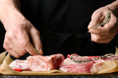 Koyu ahşap masada çiğ domuz eti hazırlayan adam.