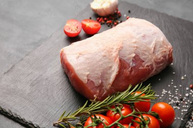 Koyu arkaplanda çiğ domuz eti, baharat ve domates tabağı, yakın plan.