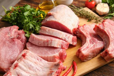 Tahta arka planda çiğ domuz eti, maydanoz ve kırmızı biber dilimleri, yakın plan.