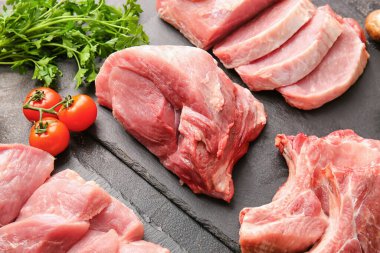 Koyu arkaplanda çiğ domuz eti, maydanoz ve domates dilimleri.