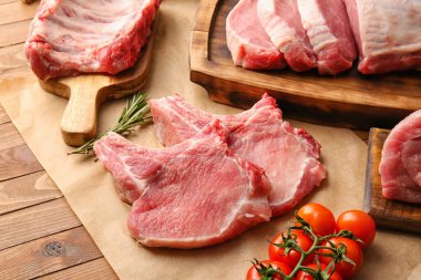 Ahşap zemin üzerinde çiğ domuz eti, biberiye ve domates dilimli parşömen.