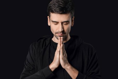 Dindar genç adam karanlık arka planda dua ediyor.