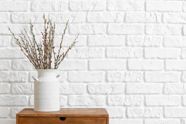 Tuğla duvarın yanındaki masada söğüt dalları olan vazo.