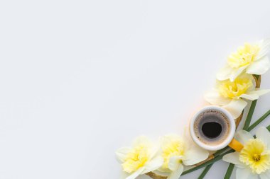 Bir fincan kahve ve beyaz arka planda güzel narsis çiçekleri.