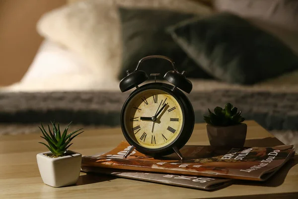 夜の寝室のテーブルの上に雑誌や観葉植物と目覚まし時計 — ストック写真