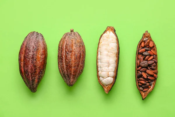 Fresh cocoa fruits and beans on color background