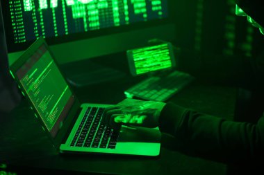 Karanlık odada bilgisayar kullanan cep telefonu olan bir bilgisayar korsanı