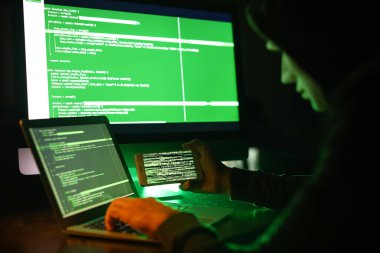 Karanlık odada bilgisayar kullanan cep telefonu olan bir bilgisayar korsanı.