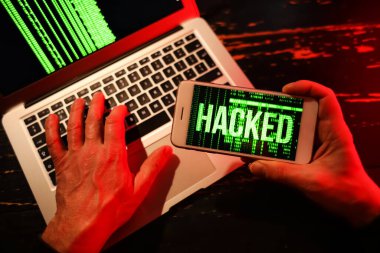 Koyu arkaplanda cep telefonu ve dizüstü bilgisayarı olan bilgisayar korsanlarının elleri