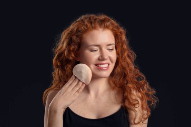 Koyu arkaplanda makyaj süngeri olan güzel bir genç kadın.