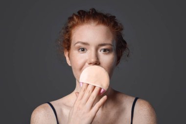 Koyu arkaplanda makyaj süngeri olan güzel bir genç kadın.