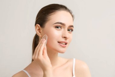 Gri arka planda makyaj süngeri olan güzel bir genç kadın.