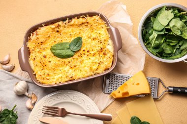 Lezzetli yeşil lazanyalı fırın yemeği ve renkli arka planda malzemeler.