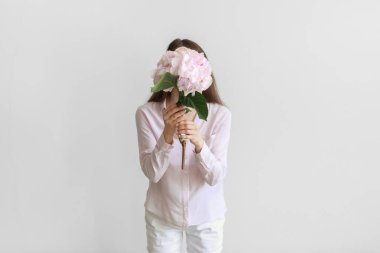 Açık arkaplanda ortanca çiçekleri olan genç bir kadın.