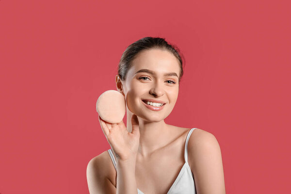 Beautiful young woman with makeup sponge on color background