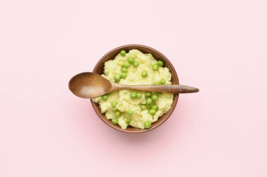 Bir kase patates püresi, yeşil bezelye ve arka planda kaşık.