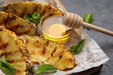 Izgara ananas dilimleri ve koyu arkaplanda bal olan tahta, yakın plan.