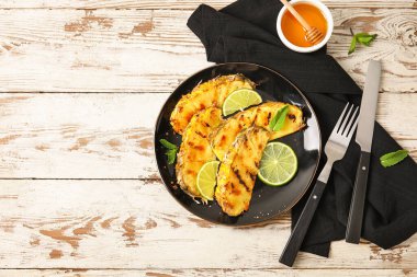 Izgara ananas dilimleri ve hafif ahşap arka planda bal tabağı.