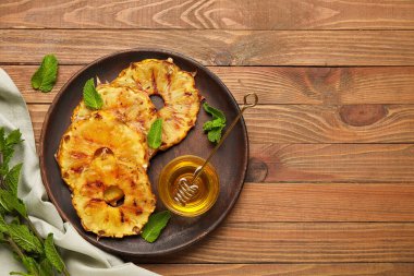 Izgara ananas dilimleri ve ahşap zemin üzerinde bal olan bir tabak.