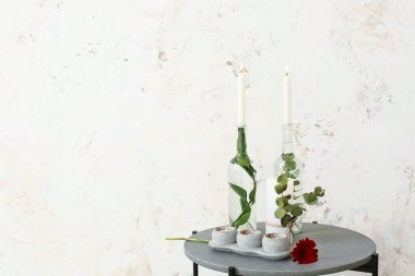 Işık duvarının yanındaki masada çiçek ve bitki dalları olan mumlar.