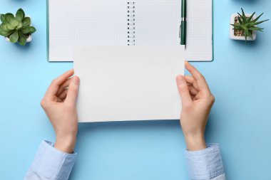 Renkli arka planda boş kağıt, defter, kalem ve ev bitkilerine sahip kadın elleri