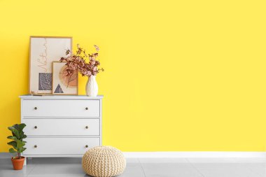 Renkli duvarın yanındaki çekmecelerin üzerinde çiçek açan dallar olan vazo.