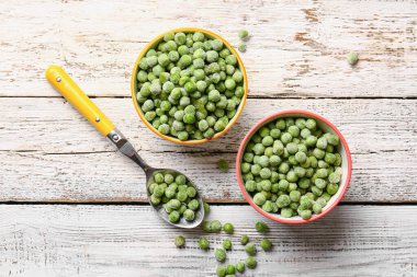 Hafif ahşap arka planda donmuş yeşil bezelyeler ve kaşıklar.
