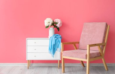 Çekmeceli sandıkta ortanca çiçekleri ve renk duvarının yanında koltuk olan vazo.