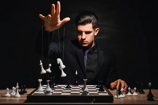 暗い背景にテーブルの上に文字列とチェスの駒を持つ男 — ストック写真