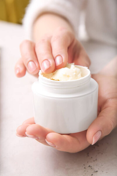 Female hands with jar of shea butter on light background, closeup
