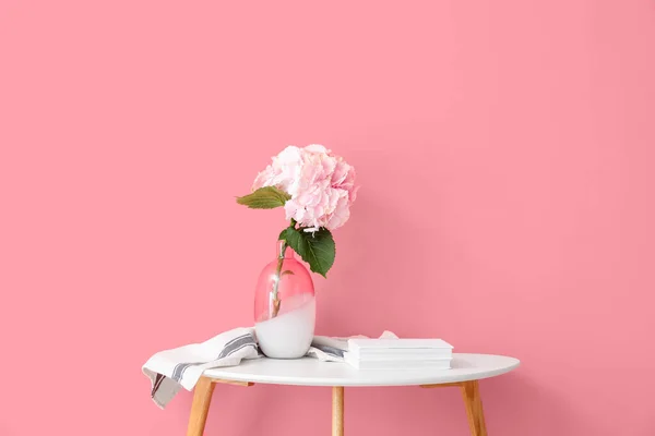 Vase with beautiful hydrangea flowers and books on table near color wall