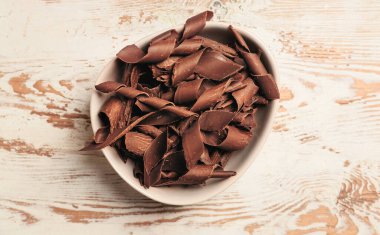 Beyaz ahşap arka planda lezzetli çikolata bukleleri olan kase.