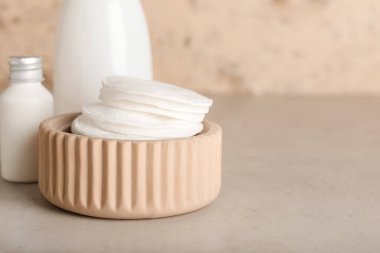 Bowl with cotton pads and bottles of cosmetic products on light background, closeup
