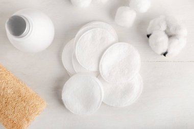 Cotton pads, flower and bottle of cosmetic product on light background